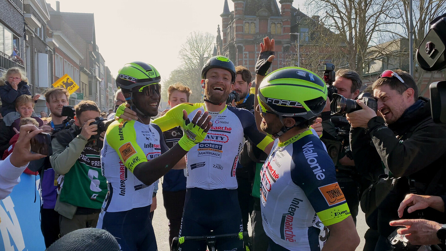 Des cyclistes sur route célèbrent à la ligne d'arrivée, entourés de photographes et de fans.